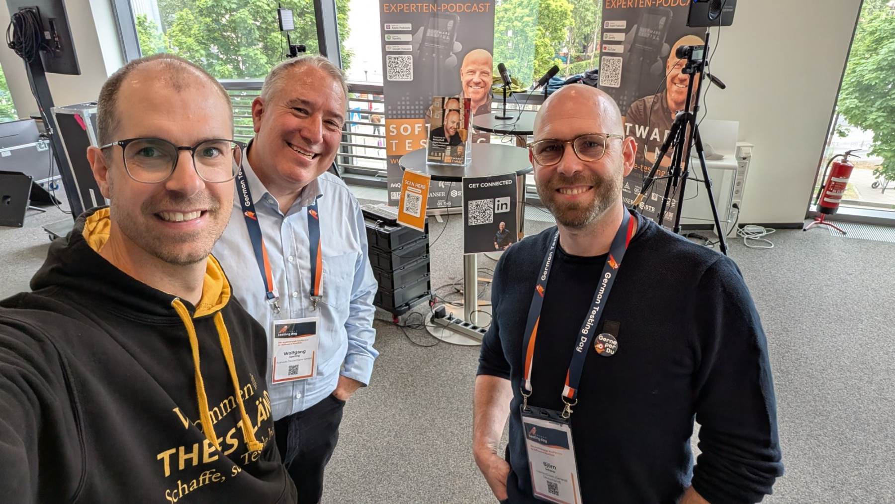 Selfie von Matthias Groß, Wolfgang Sperling und Björn Scherer vor einem Podcast-Stand beim German Testing Day 2026.