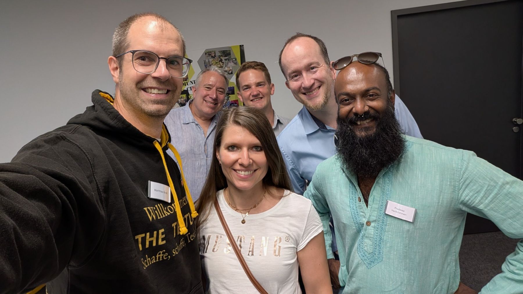 Gruppenselfie beim Come Together: Matthias Groß im schwarzen TestLänd-Kapuzenpulli mit 5 weiteren lachenden Teilnehmenden, rechts Pradeep Harikrishnan mit Namensschild.