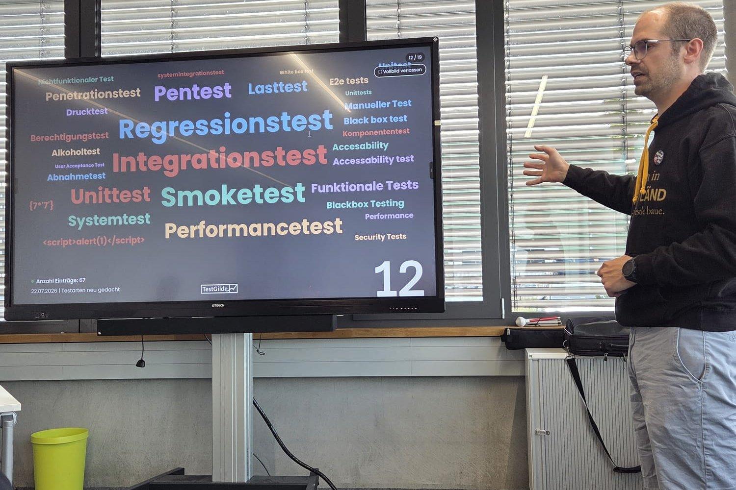 Matthias Groß zeigt auf die Live-Wortwolke mit Testarten wie Regressionstest, Integrationstest, Smoketest und Pentest. Unten links stehen die Eingaben {7*7} und <script>alert(1)</script> als normaler Text.
