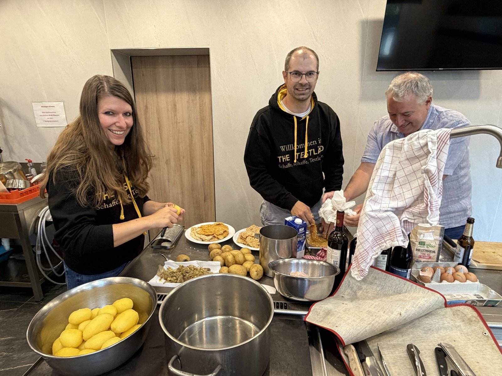 3 Teilnehmende in der Küche des Selbstversorgerhauses beim Panieren von Schnitzeln und Schälen von Kartoffeln, 2 davon in schwarzen Kapuzenpullis vom TestLänd.