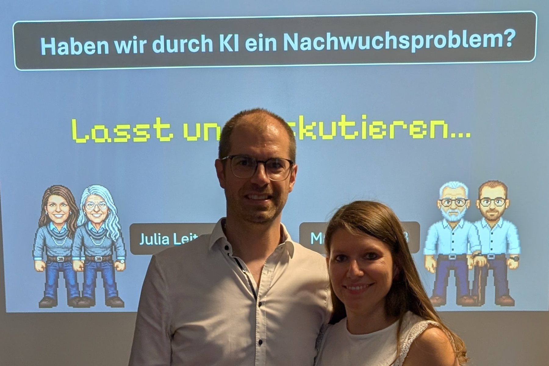 Julia Leitner und Matthias Groß, die beiden Moderierenden der Diskussionsrunde, vor der Titelfolie mit ihren Pixel-Avataren in jung und alt.