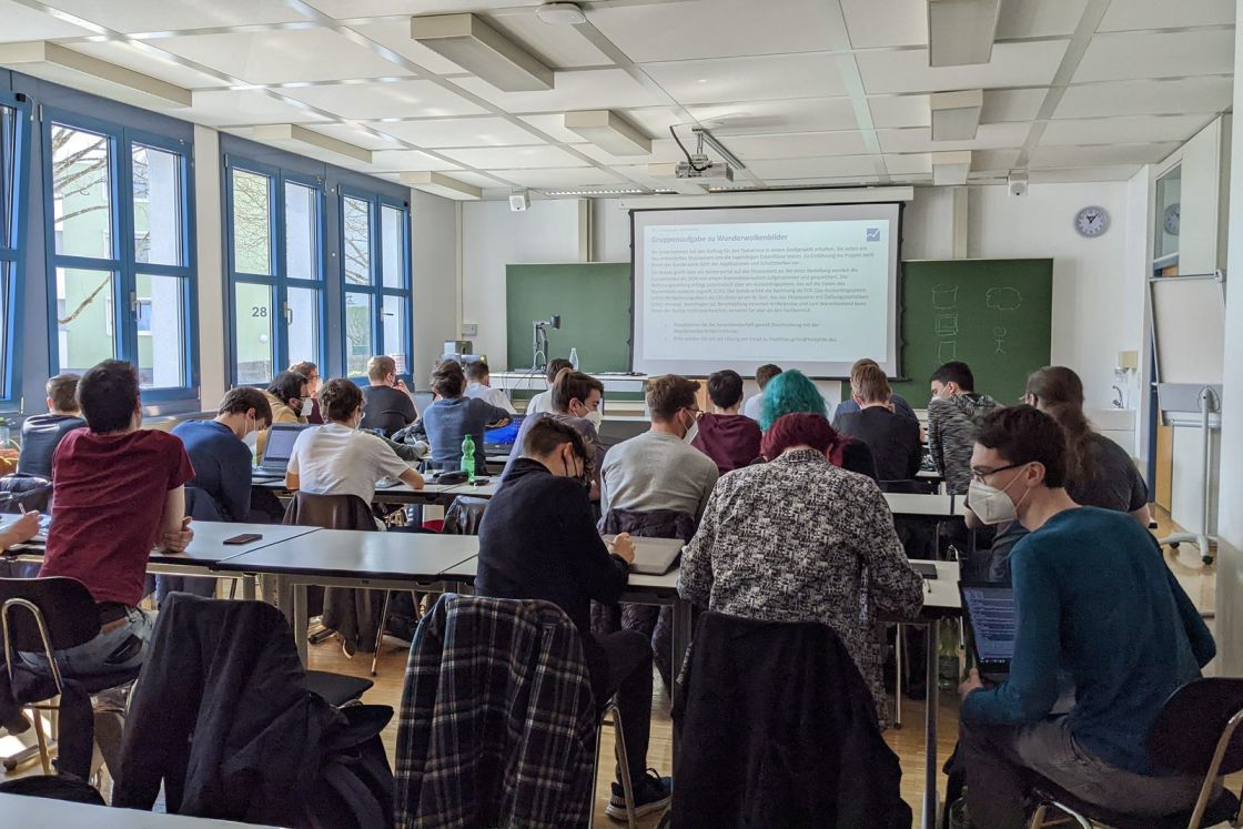 Studierende sitzen von hinten fotografiert in einem Hörsaal der DHBW vor einer Tafel mit Projektion.