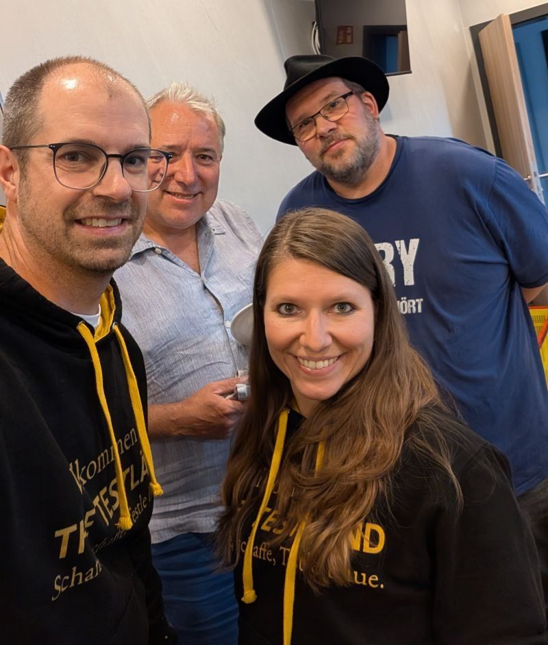 Selfie von vier lachenden Personen, zwei davon tragen schwarze TestLänd-Kapuzenpullover.